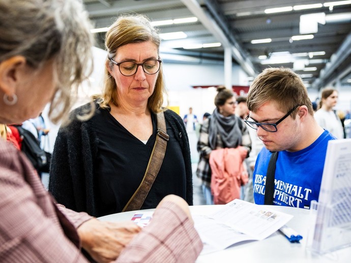 Eine Frau und ein jüngerer Mann lassen sich an einem Messestand beraten. (vergrößerte Bildansicht wird geöffnet)