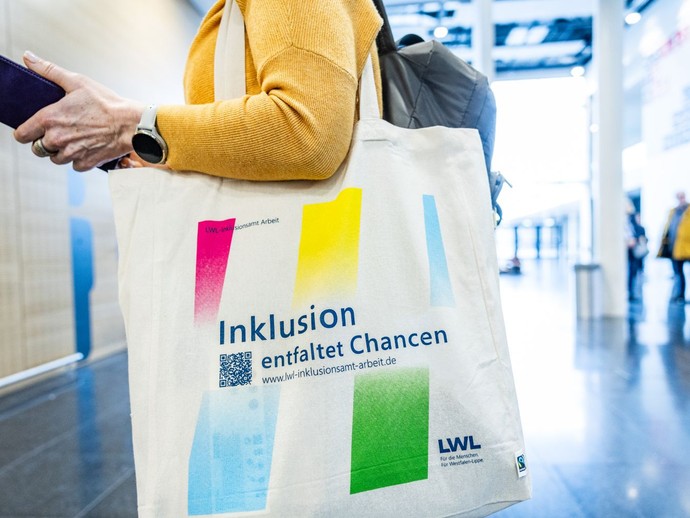Eine Person trägt einen Jutebeutel mit der Aufschrift „Inklusion entfaltet Chancen“. (vergrößerte Bildansicht wird geöffnet)