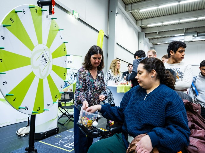 Eine Frau nimmt nach dem Drehen an einem Glücksrad eine Tüte Fruchtgummi aus einer Box. (vergrößerte Bildansicht wird geöffnet)