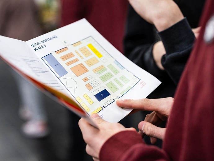 Eine Person hält einen Messeplaner in der Hand und betrachtet die Hallenübersicht. (vergrößerte Bildansicht wird geöffnet)