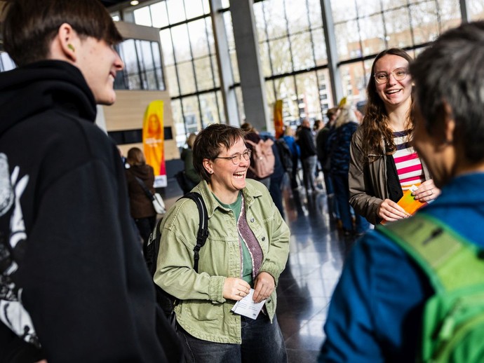 Vier Personen stehen in einem Kreis, unterhalten sich und lachen gemeinsam. (vergrößerte Bildansicht wird geöffnet)